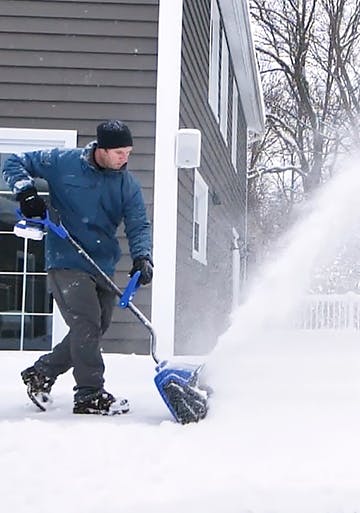 Snow Joe 24-volt Cordless 13-inch Snow Shovel being used to throw snow off a patio deck.